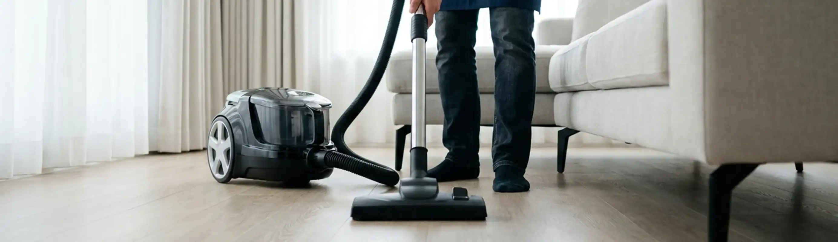 Professional house cleaner vacuuming a living room floor with a canister vacuum cleaner, Syracuse, NY.