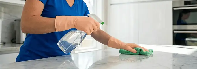 Maid service worker spraying and wiping a kitchen countertop with a microfiber cloth for sanitizing, Syracuse, NY.