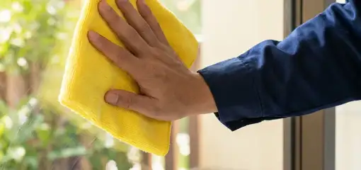 House cleaner wiping a glass window with a yellow microfiber cloth for streak-free cleaning, Syracuse, NY.